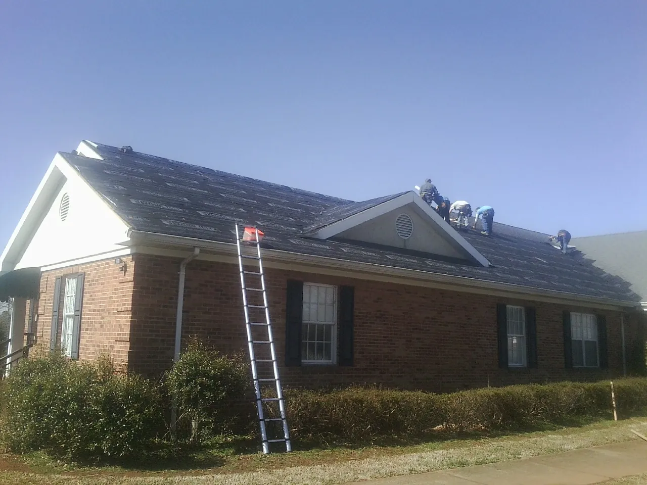 Crew tearing shingles off a brick ranch roof with a ladder set — Emergency Roof Repair work by our crew in Cape Elizabeth
