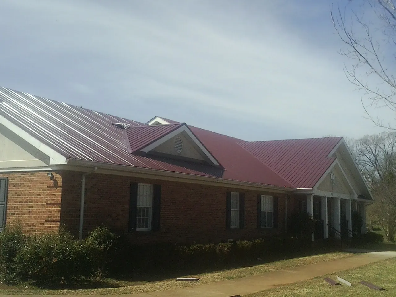 Red metal roof with gabled entries on a long brick building, from a Hail Damage Roof Repair job in Cape Elizabeth