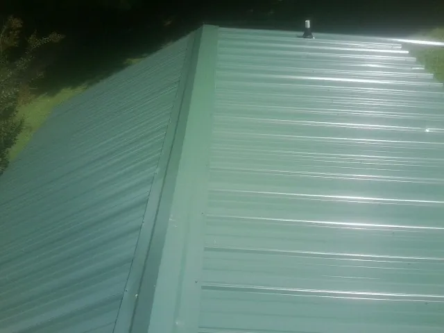 New green metal panels meeting at the ridge of a roof — Flat Roof Repair work by our crew in Cape Elizabeth