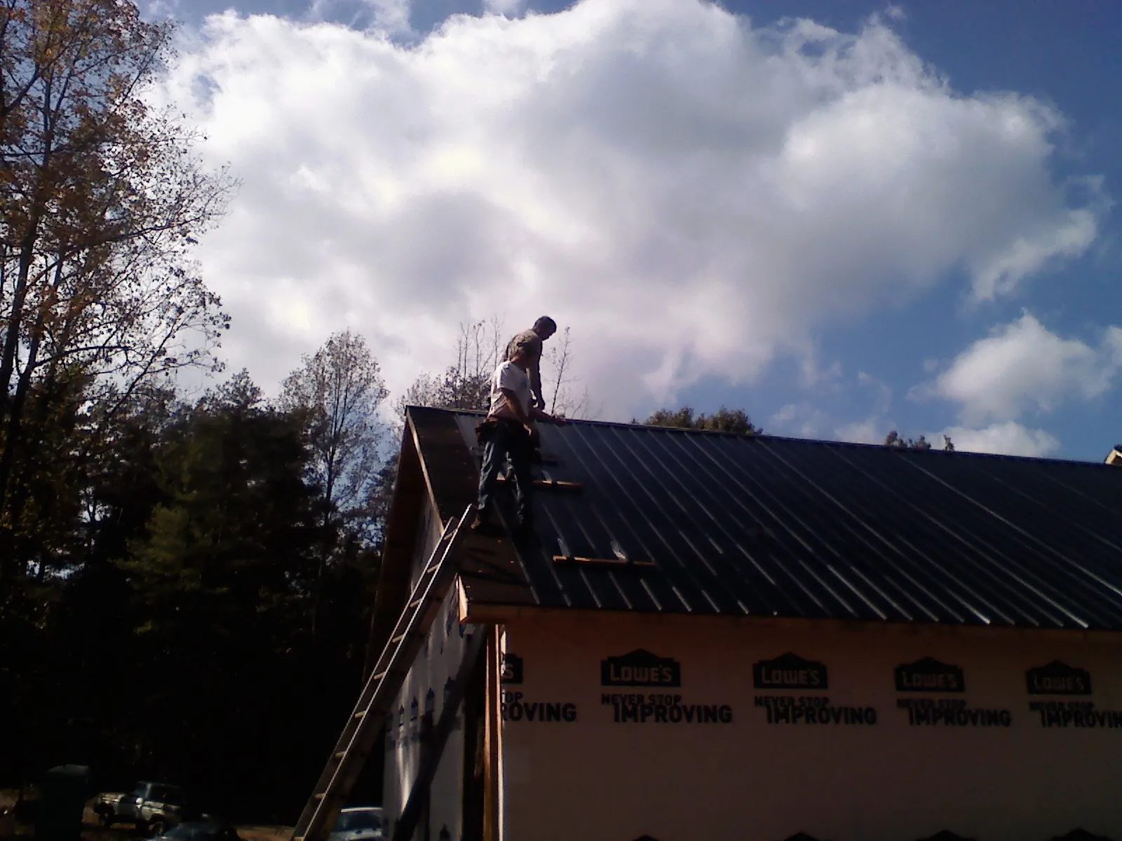 Roofer fastening dark metal panels high against a cloudy sky, from a Roof Inspection job in Cape Elizabeth