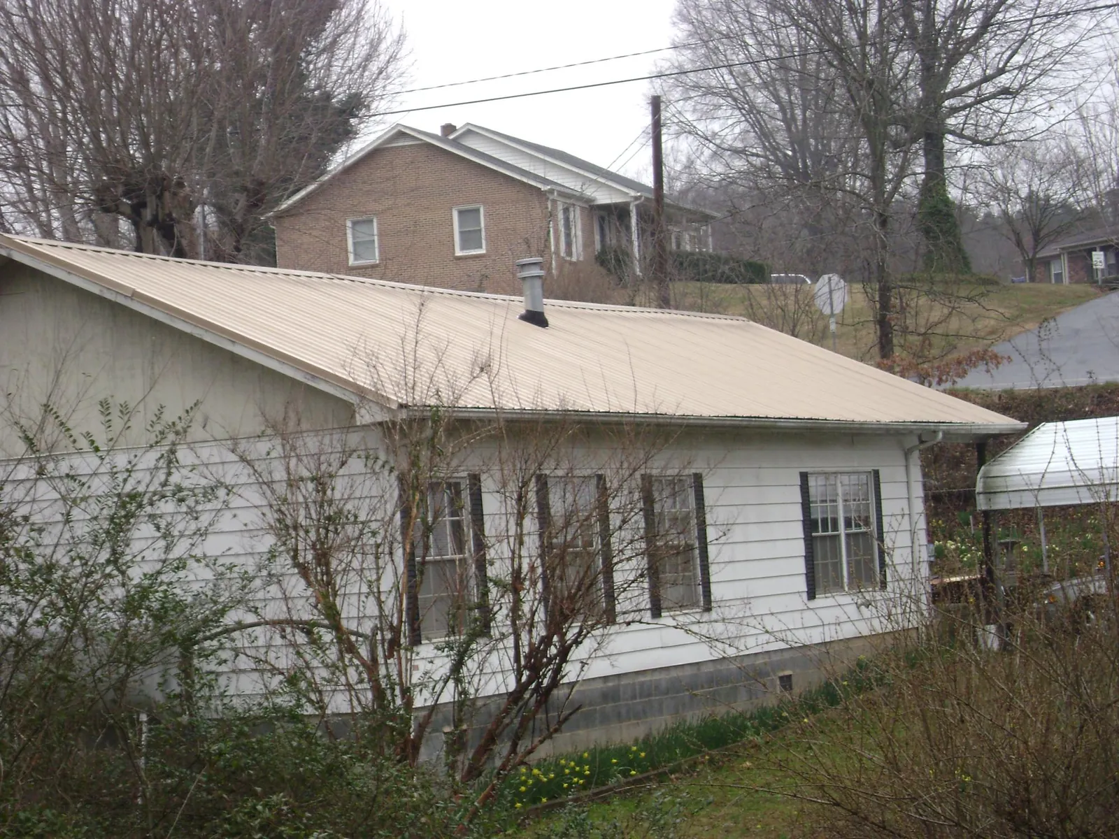 Tan metal roof on a white sided house set into a hillside — Commercial Roofing by Roofing Brothers in Cape Elizabeth