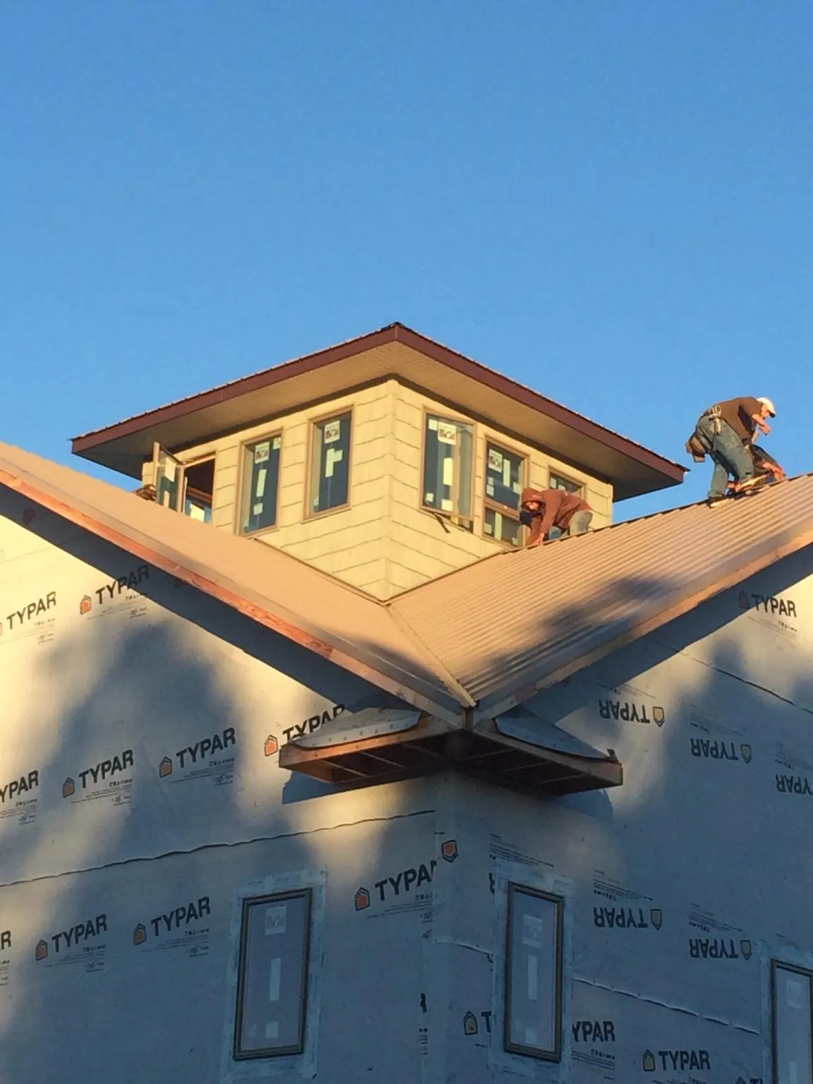 Roofers working around a rooftop cupola on a new metal roof at sunset — Roof Waterproofing in Cape Elizabeth by Roofing Brothers
